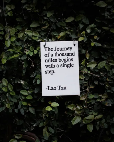 A sign hanging on a leafy wall with a quote from Lao Tzu: The Journey of a thousand miles begins with a single step.